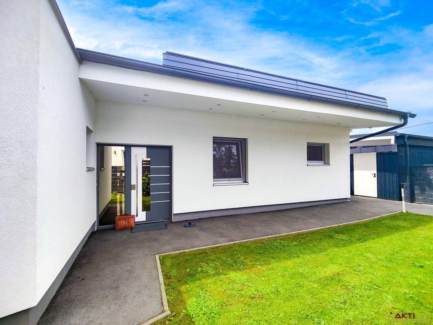 Moderner Hauseingang mit weißer Fassade und gepflegtem Rasenbereich.