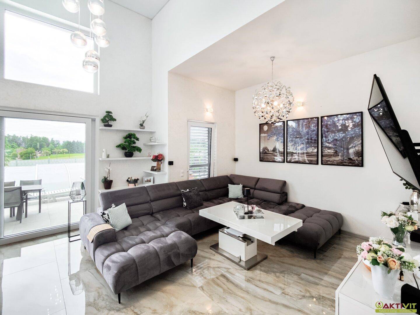Großzügiges Wohnzimmer mit hoher Decke, moderner Couch und Zugang zur Terrasse.