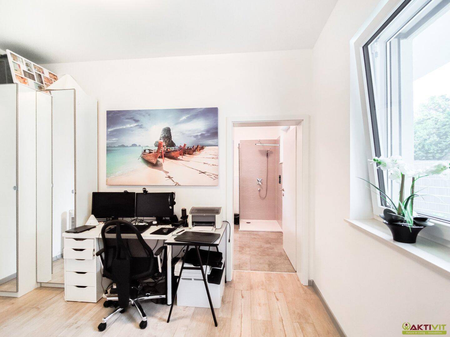 Helles Arbeitszimmer mit Schreibtisch, Schränken und Blick ins Grüne.