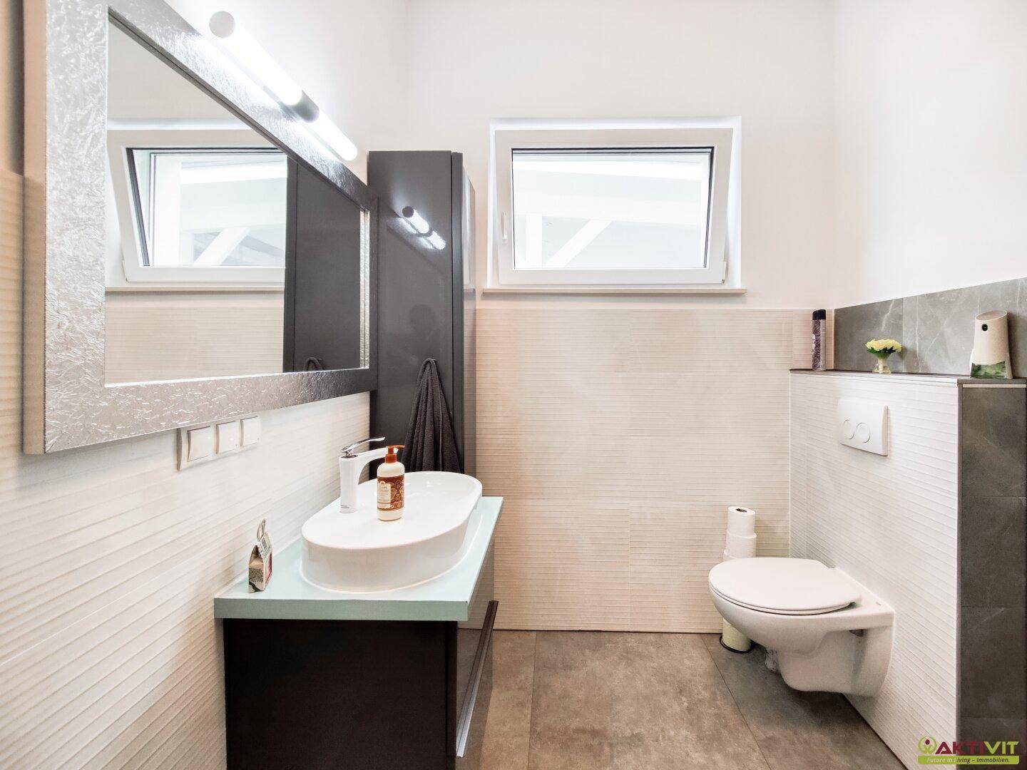 Modernes Badezimmer mit Einzelwaschbecken, Wand-WC und Fenster für Tageslicht.