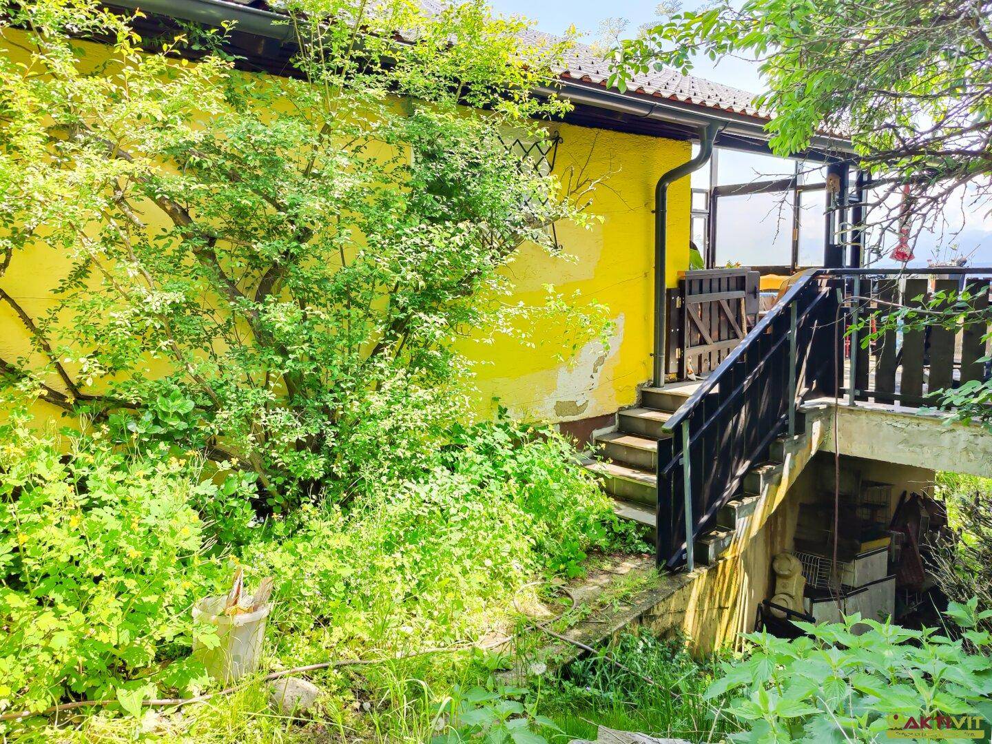 Seitenansicht des Hauses mit Außentreppe und üppiger Vegetation im Gartenbereich.
