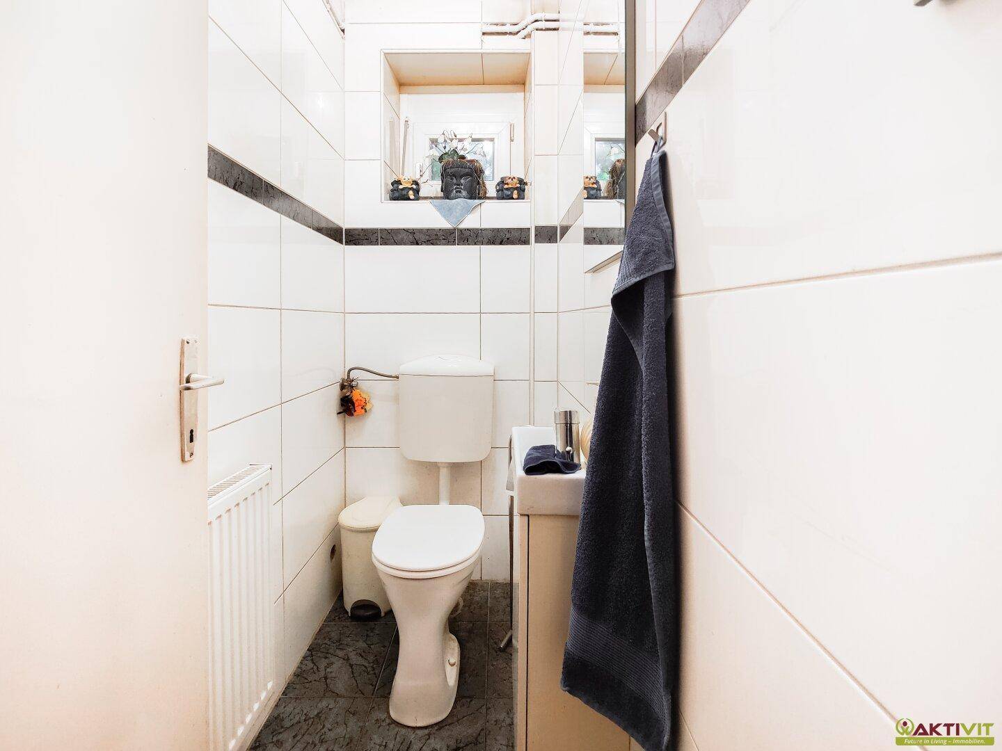Kleines Gäste-WC mit weißen Fliesen, dunklem Akzentstreifen und Fenster für Tageslicht.