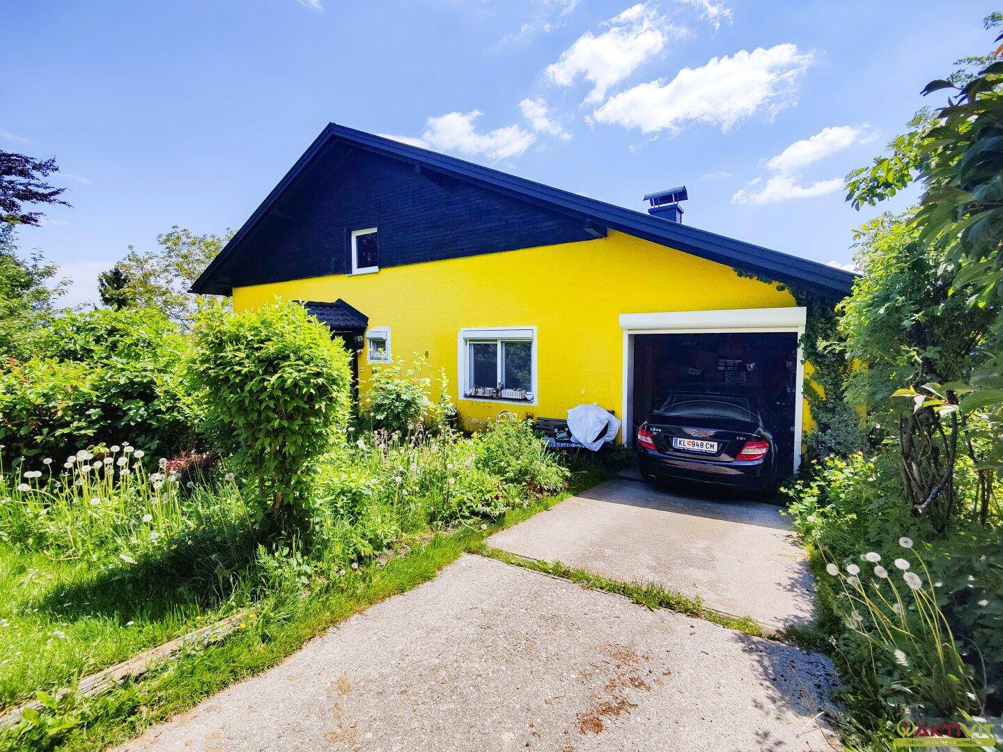 Vorderansicht des gelben Hauses mit Garage und einem gepflegten Vorgartenbereich.