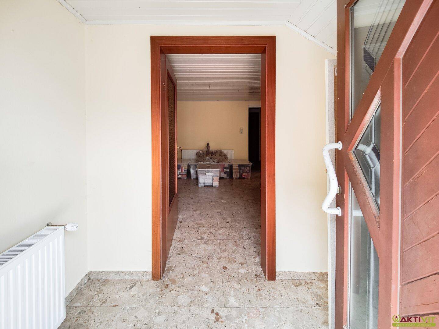 Eingangsbereich mit Fliesenboden und offener Holztür, die in einen weiteren Raum führt.