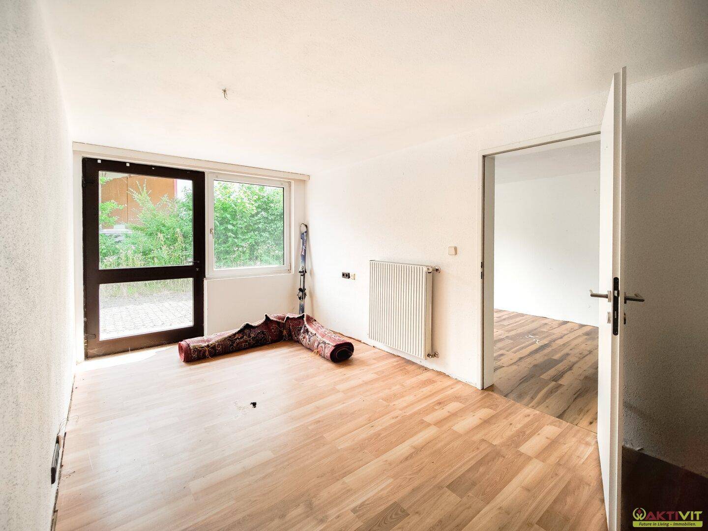 Leeres Zimmer mit Laminatboden und Zugang zu einem Außenbereich durch eine Glastür.
