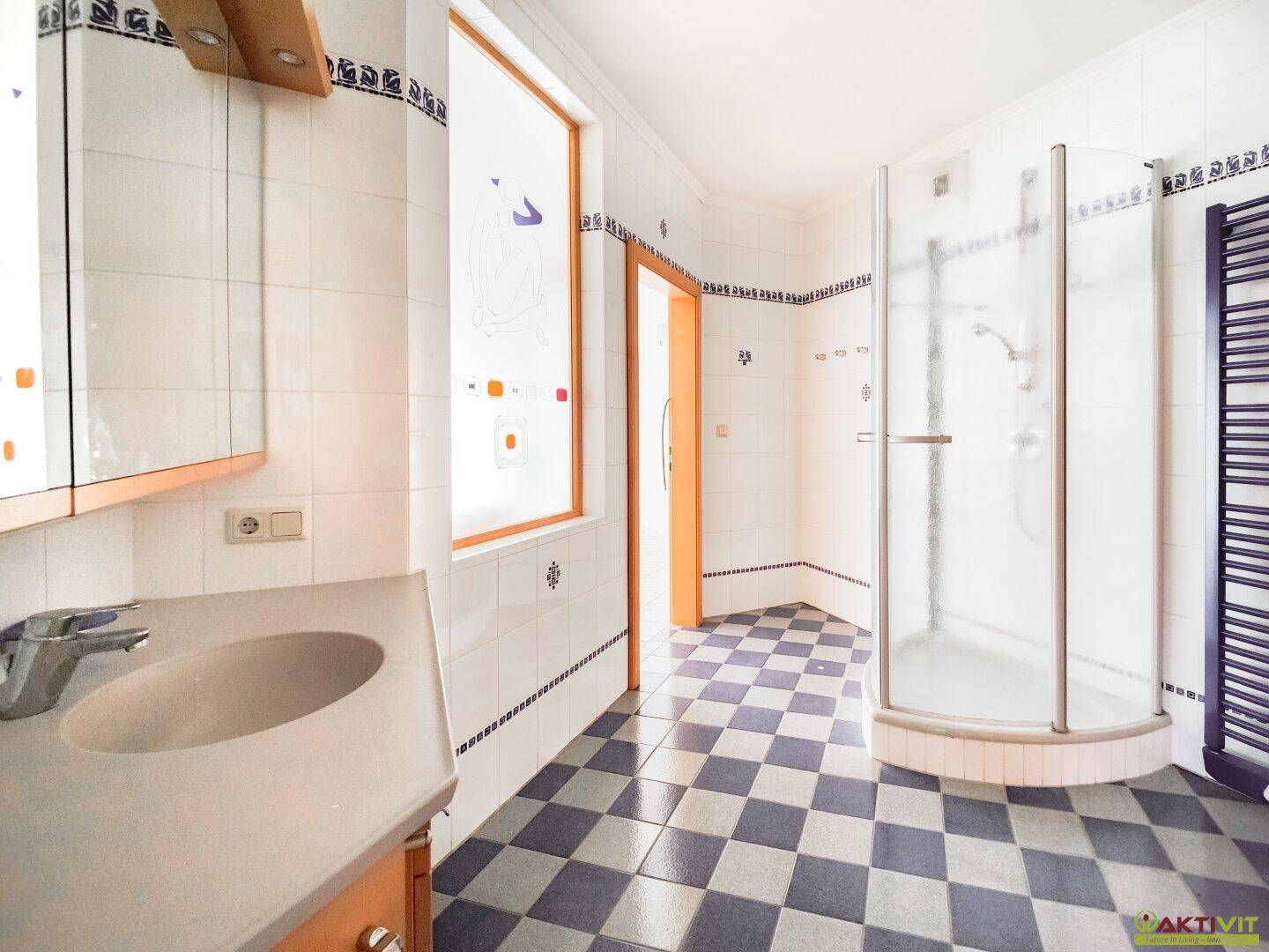 Badezimmer mit kariertem Fliesenboden, Dusche und Fenster, das Tageslicht hereinlässt.