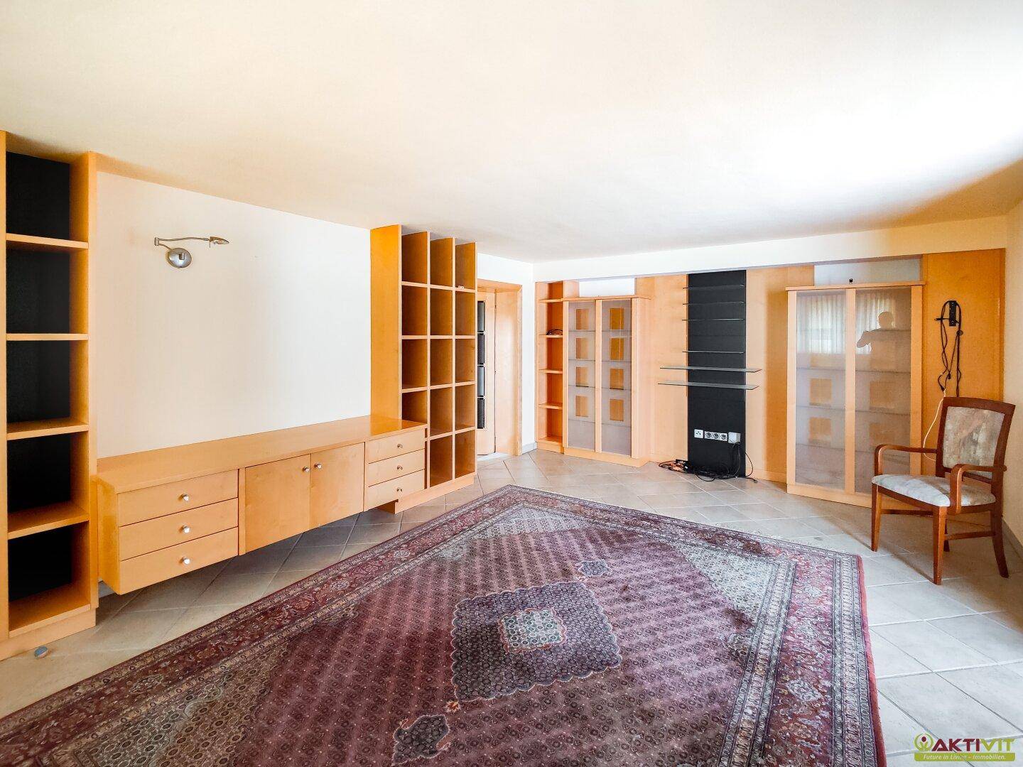 Wohnzimmer mit Einbauschränken, Regalen und einem großen Teppich, der Gemütlichkeit schafft.