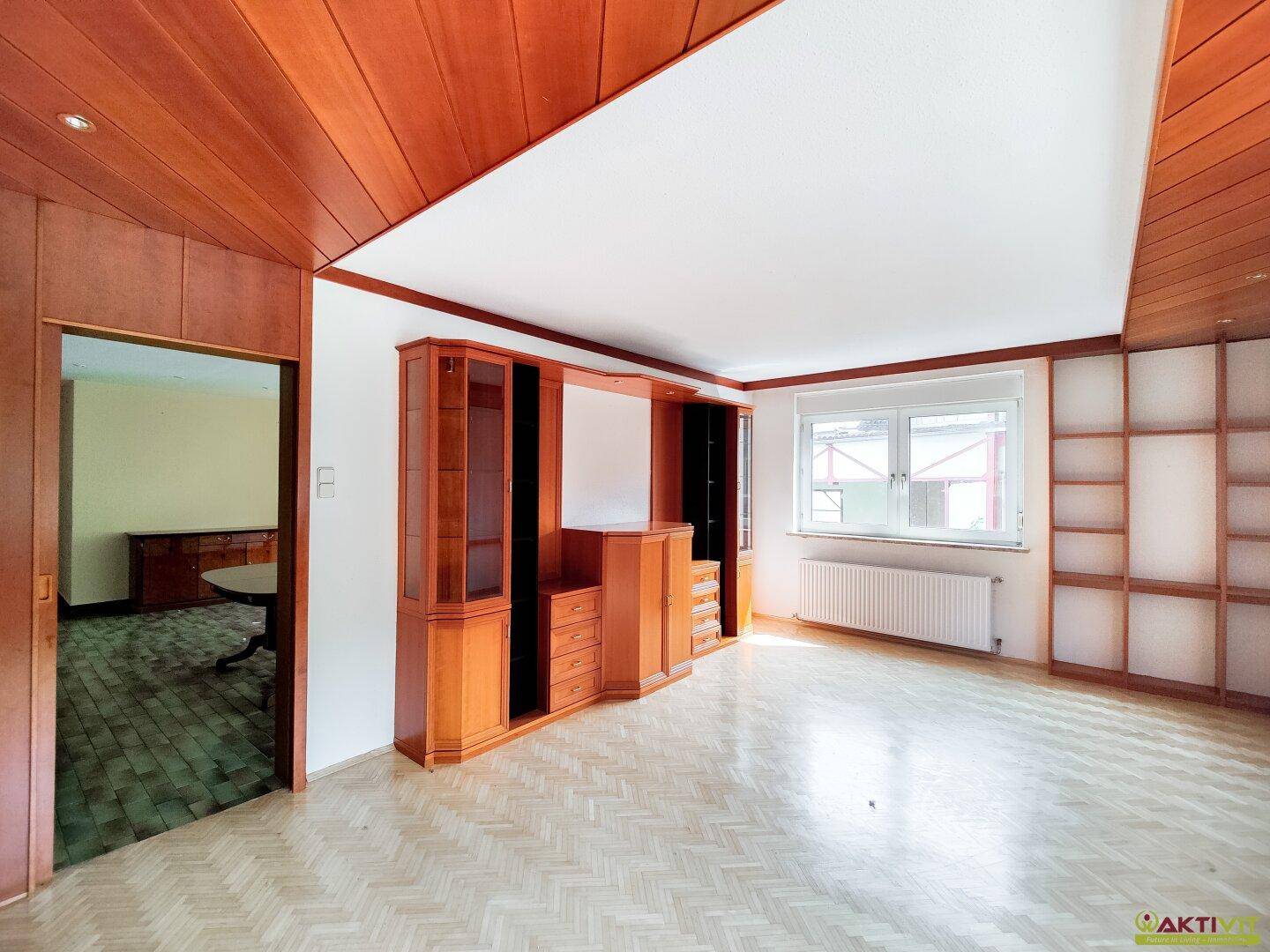 Wohnzimmer mit Holzvertäfelung an der Decke und Parkettboden, das eine warme Atmosphäre schafft.