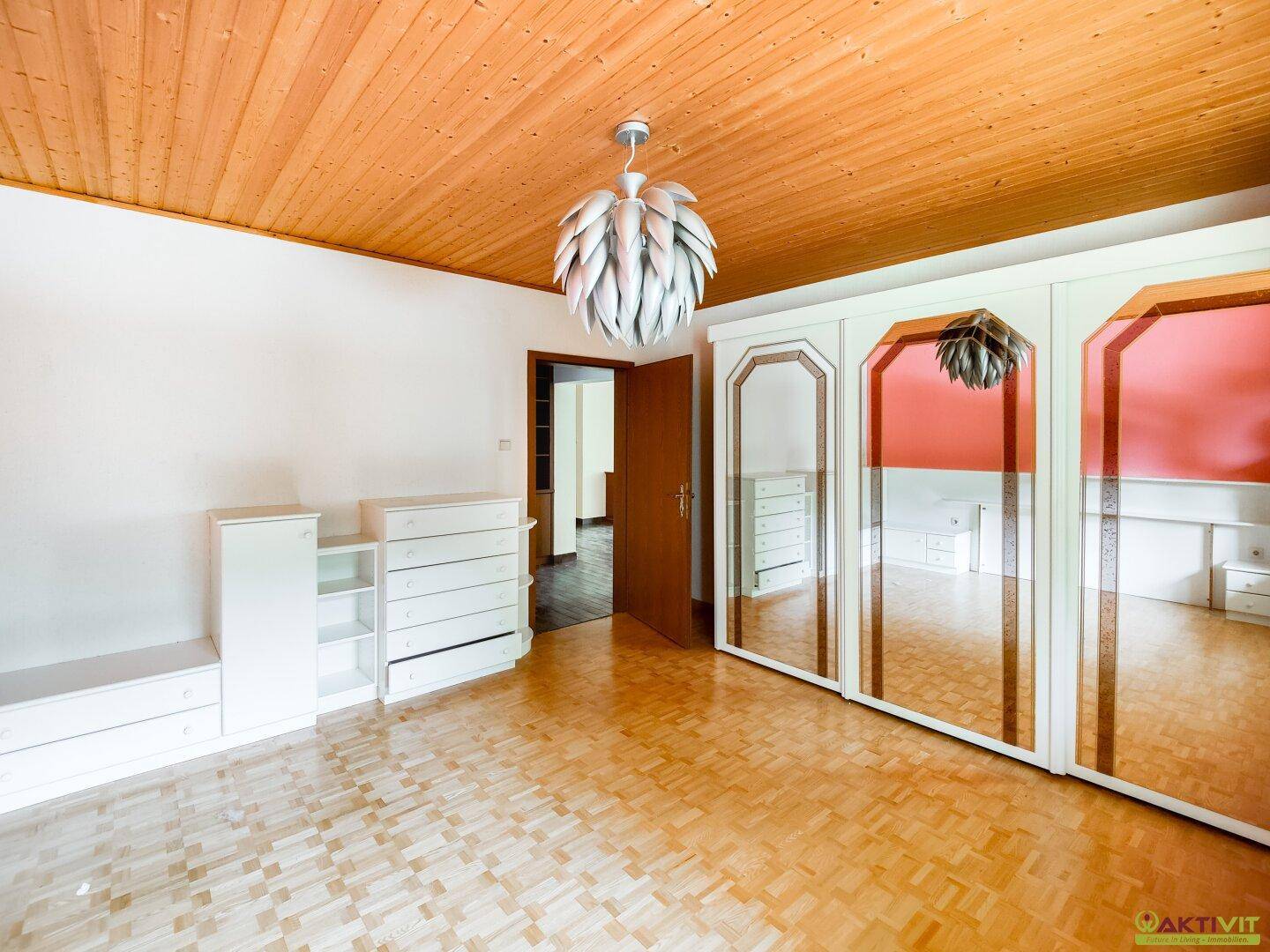 Schlafzimmer mit Holzdecke, Parkettboden und großen Spiegelschränken, die den Raum erweitern.