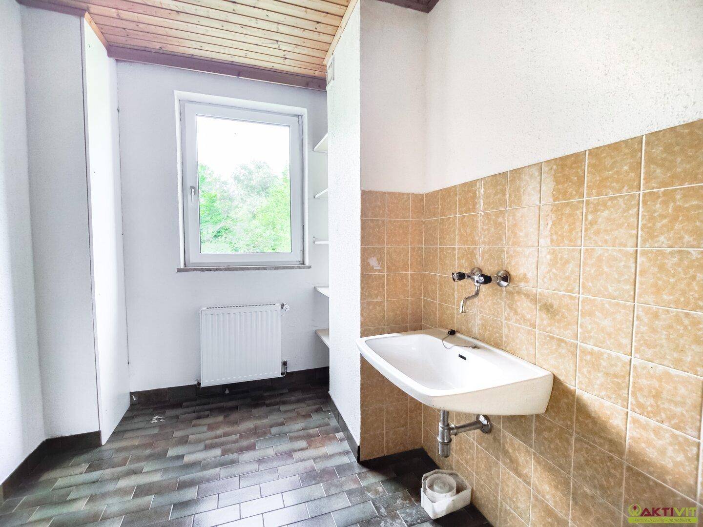 Praktischer Hauswirtschaftsraum mit Fliesenboden, Waschbecken und Fenster für natürliche Belüftung.
