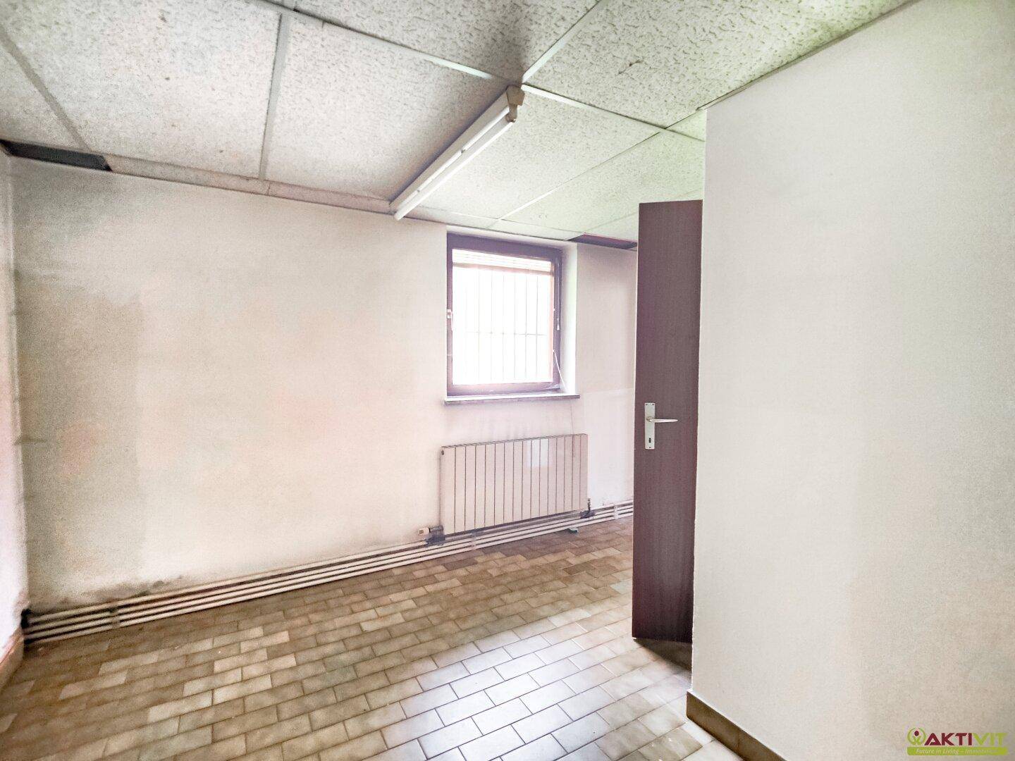 Kellerraum mit Fliesenboden, abgehängter Decke und kleinem Fenster mit Gitter.