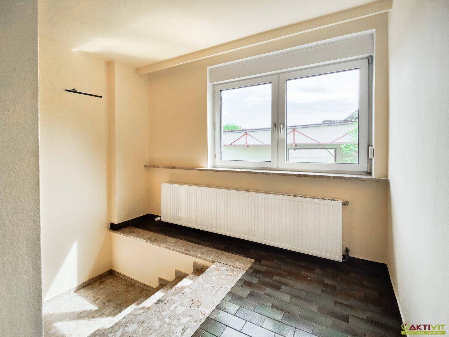 Heller Treppenabsatz mit Fliesenboden, großem Fenster und Heizkörper, der viel Licht spendet.