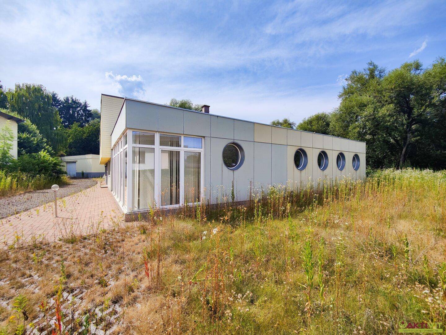 Seitenansicht des modernen Gebäudes mit runden Fenstern und großer Glasfassade in grüner Umgebung.