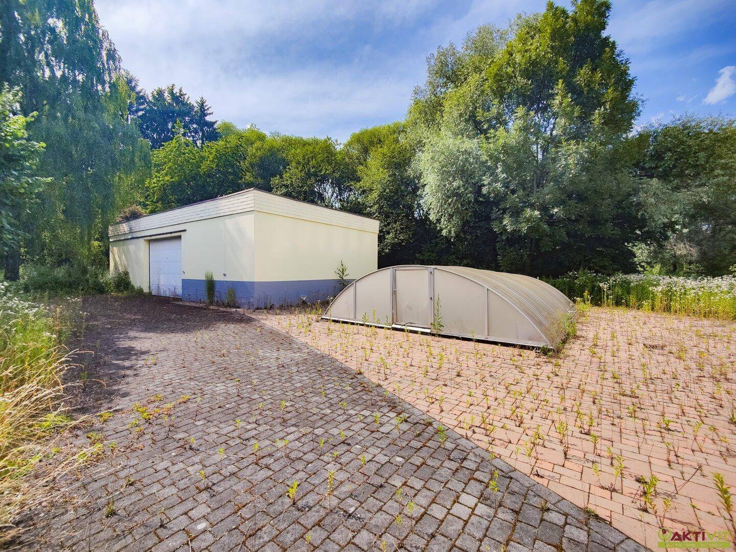 Großer Außenbereich mit gepflasterter Fläche, überdachtem Pool und einem Nebengebäude.