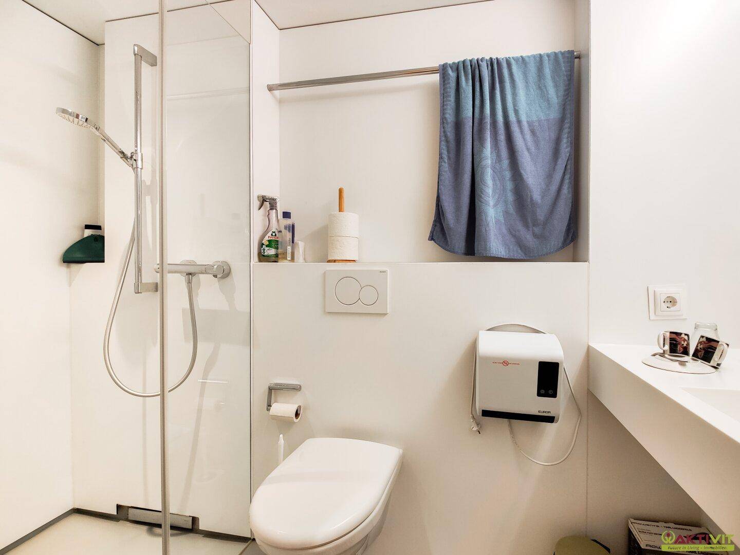 Modernes, hell gefliestes Badezimmer mit Duschkabine, Toilette und Ablagefläche.