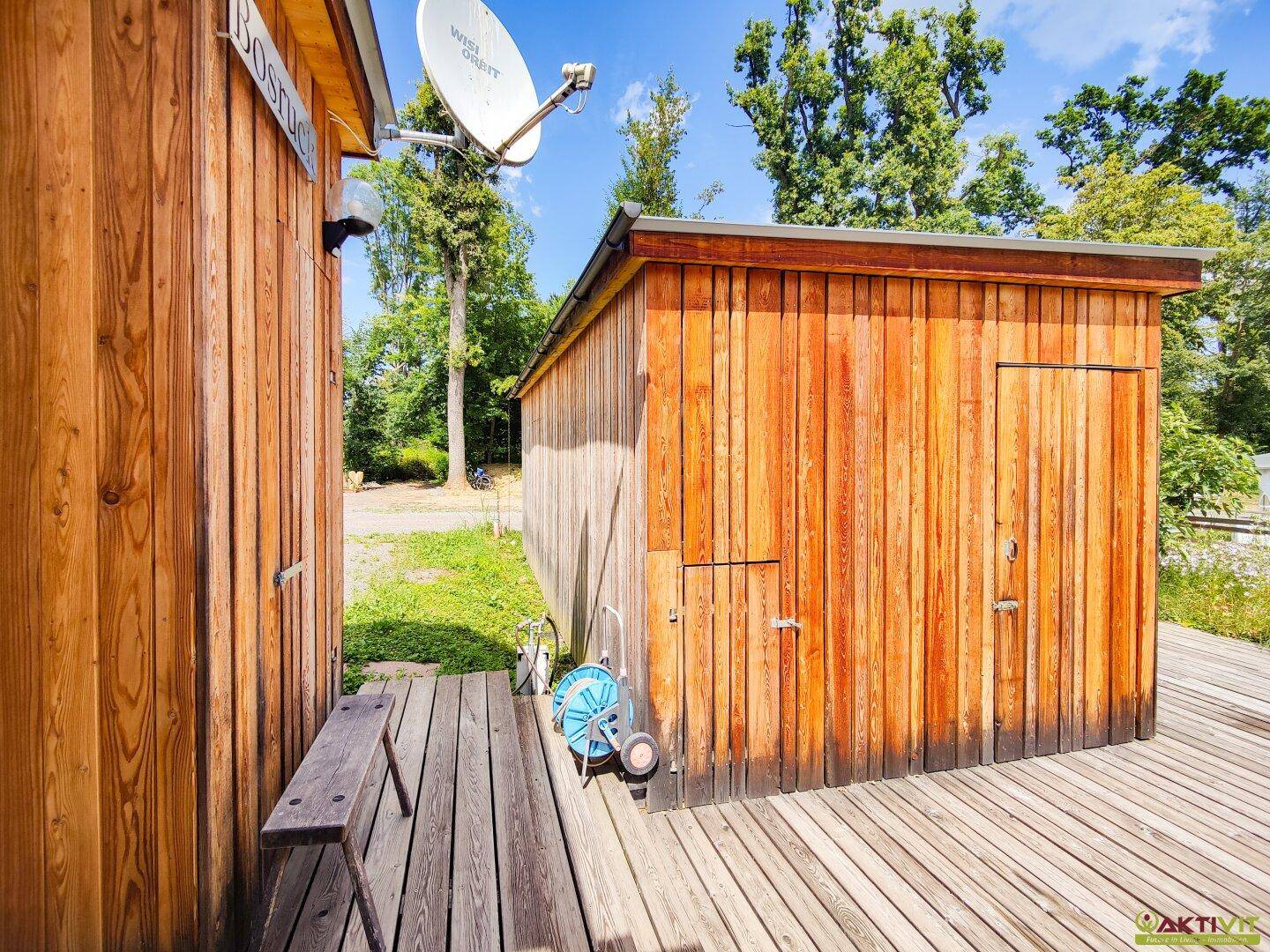 Zwei kleine Holzhütten mit einer Holzterrasse und einem Gartenschlauch auf dem Boden.