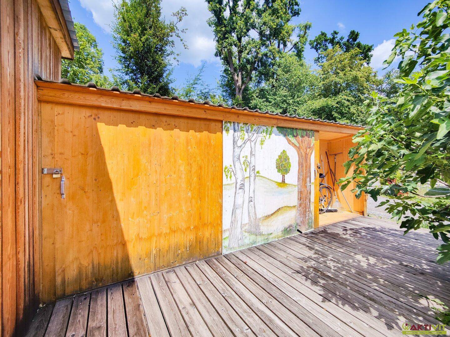Seitenansicht einer Holzhütte mit einer bemalten Schiebetür, die eine Landschaft darstellt.