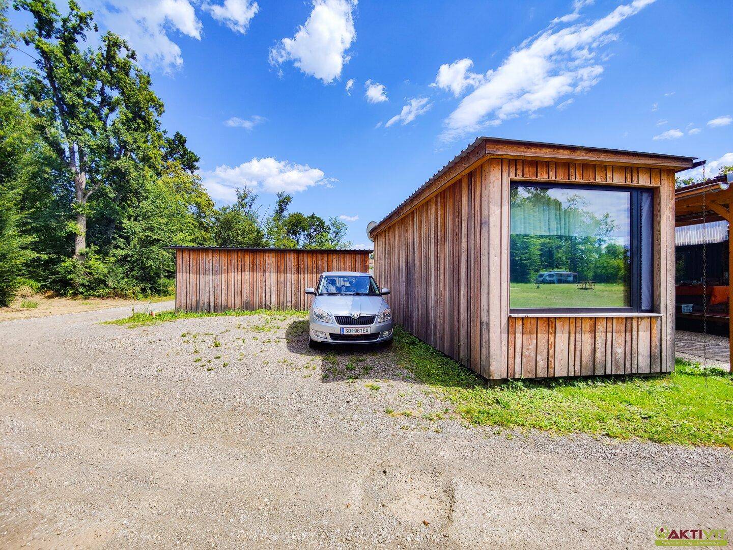Außenansicht einer Holzhütte mit großem Fenster und einem geparkten Auto davor.