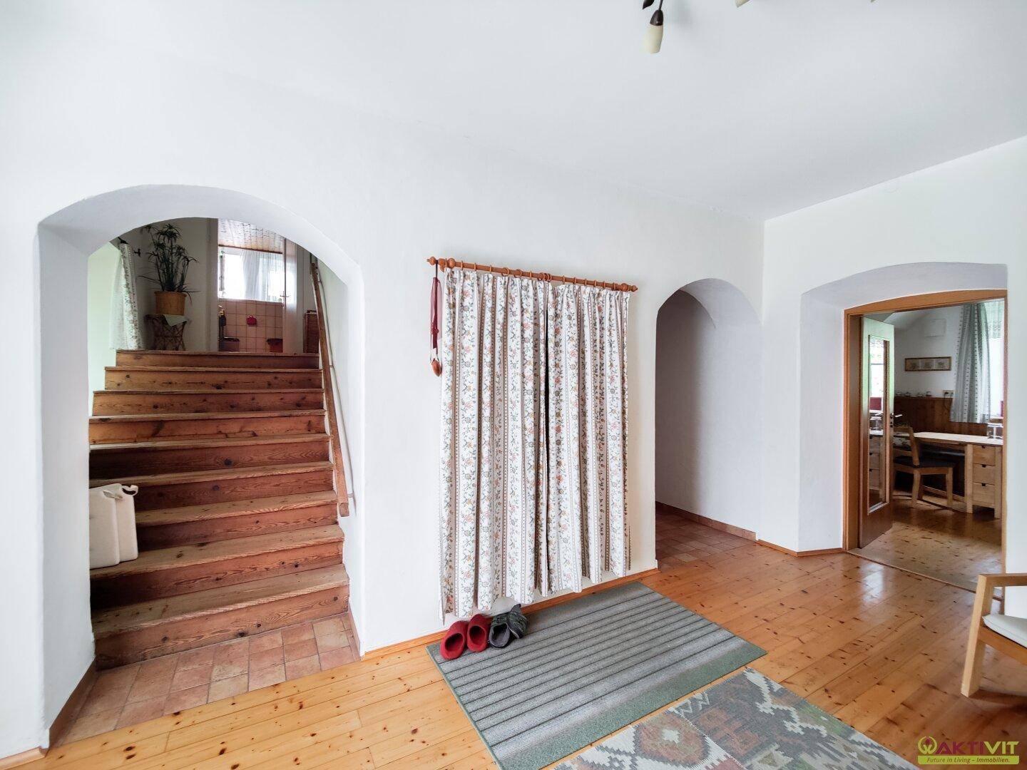 Geräumiger Flur mit Holztreppe und Rundbögen, der verschiedene Bereiche des Hauses verbindet.