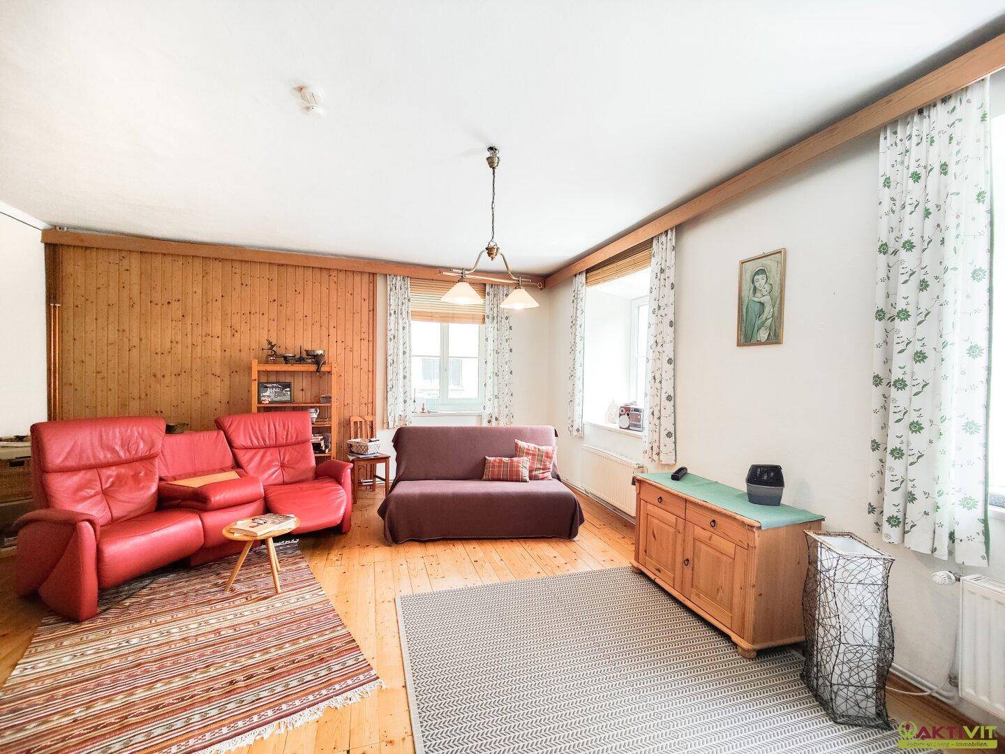 Gemütliches Wohnzimmer mit Holzvertäfelung, roten Ledersofas und traditionellem Holzboden.