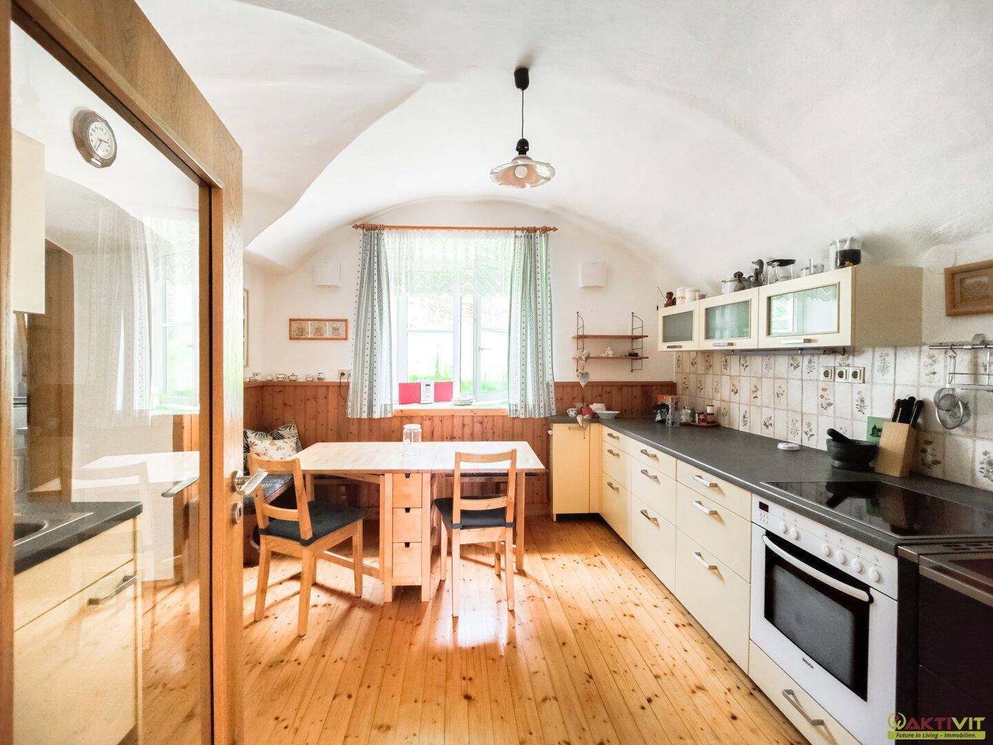 Helle Küche mit Gewölbedecke, Holzboden und traditionellen Küchenschränken, inklusive Esstisch.