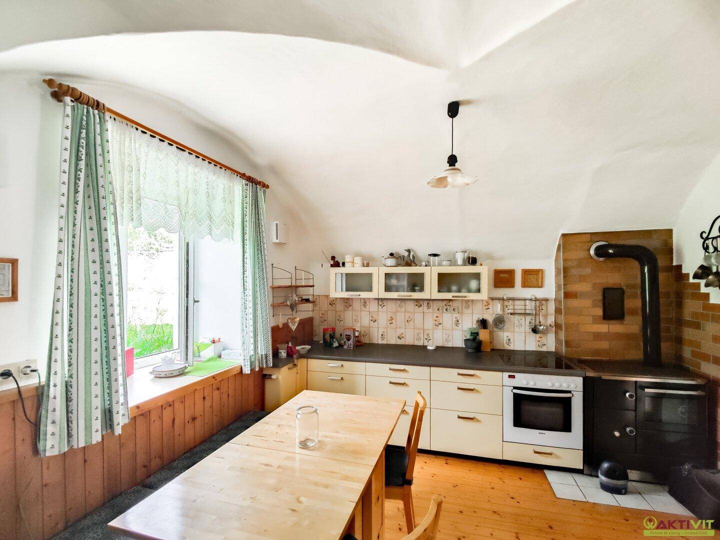 Rustikale Küche mit Gewölbedecke, Holzherd und Esstisch, bietet eine gemütliche Kochumgebung.
