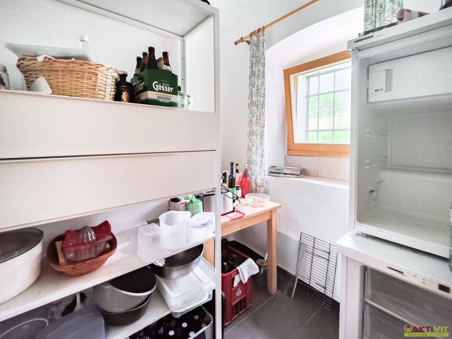 Praktische Speisekammer mit Regalen, Kühlschrank und kleinem Fenster für zusätzliche Belüftung.