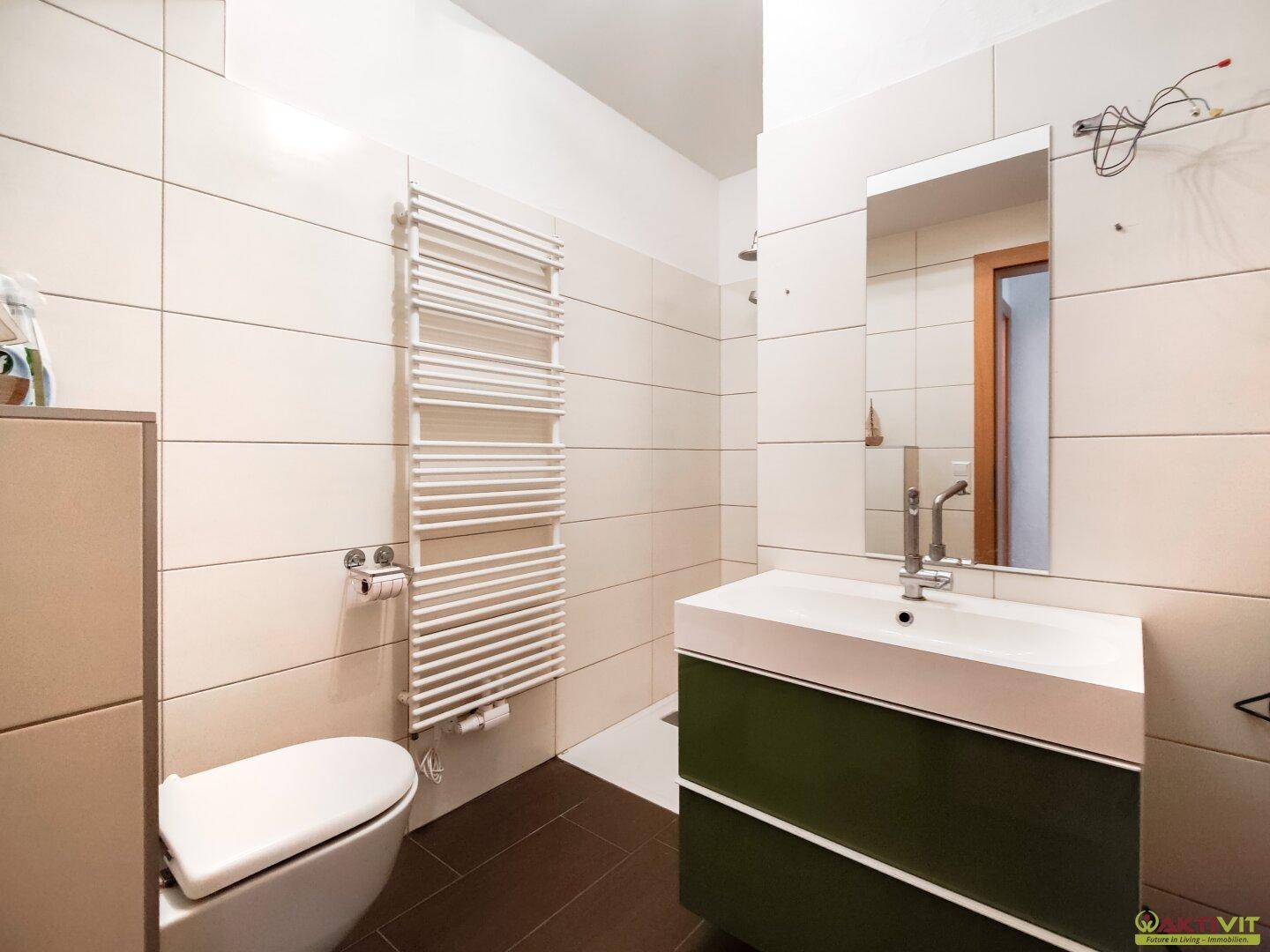 Modernes Badezimmer mit beigefarbenen Fliesen, Waschtisch und beheiztem Handtuchhalter.