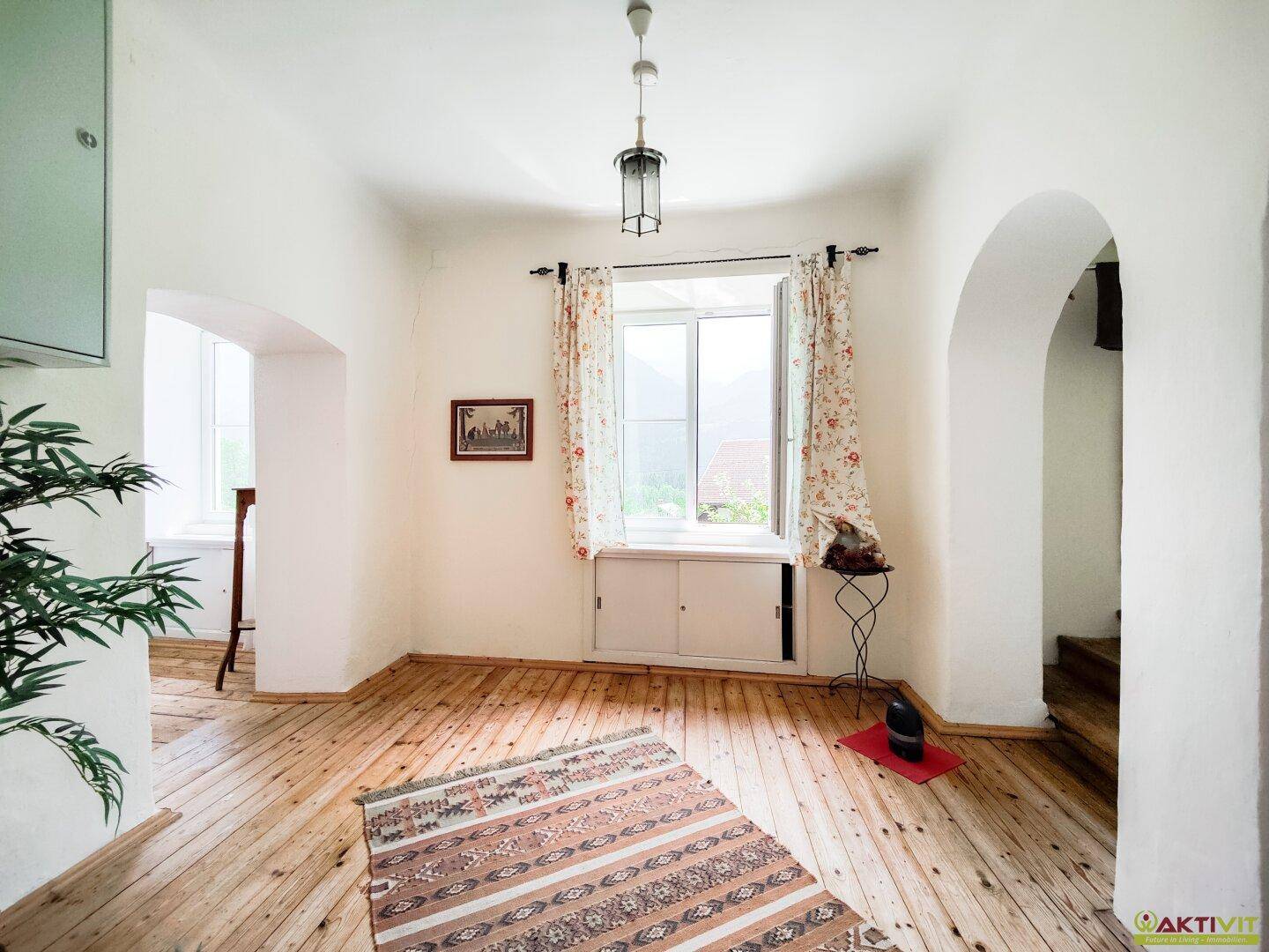 Geräumiger Flur mit Holzboden, Fenster und Zugang zu weiteren Zimmern durch Rundbögen.