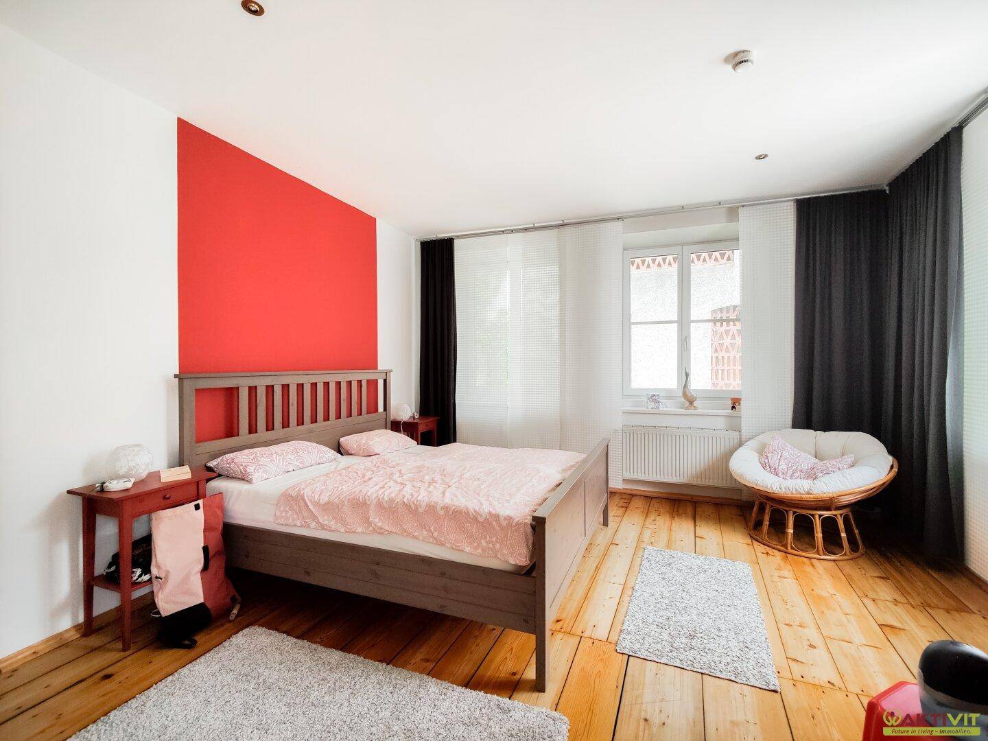 Helles Schlafzimmer mit Holzbett, roter Akzentwand und Holzboden, bietet eine gemütliche Atmosphäre.
