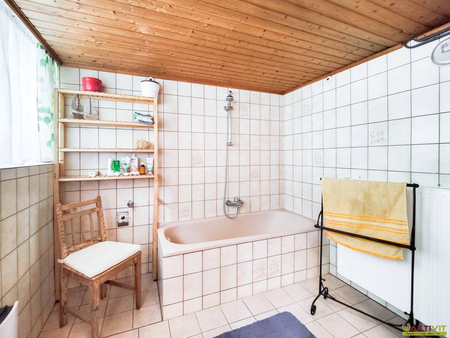 Traditionelles Badezimmer mit Badewanne, weißen Fliesen und Holzdecke, bietet eine funktionale Ausstattung.