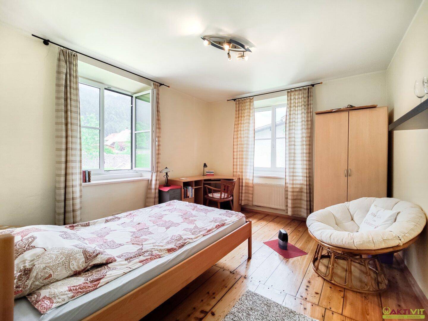 Gemütliches Schlafzimmer mit Holzboden, Schreibtisch und großem Fenster, das viel Licht spendet.
