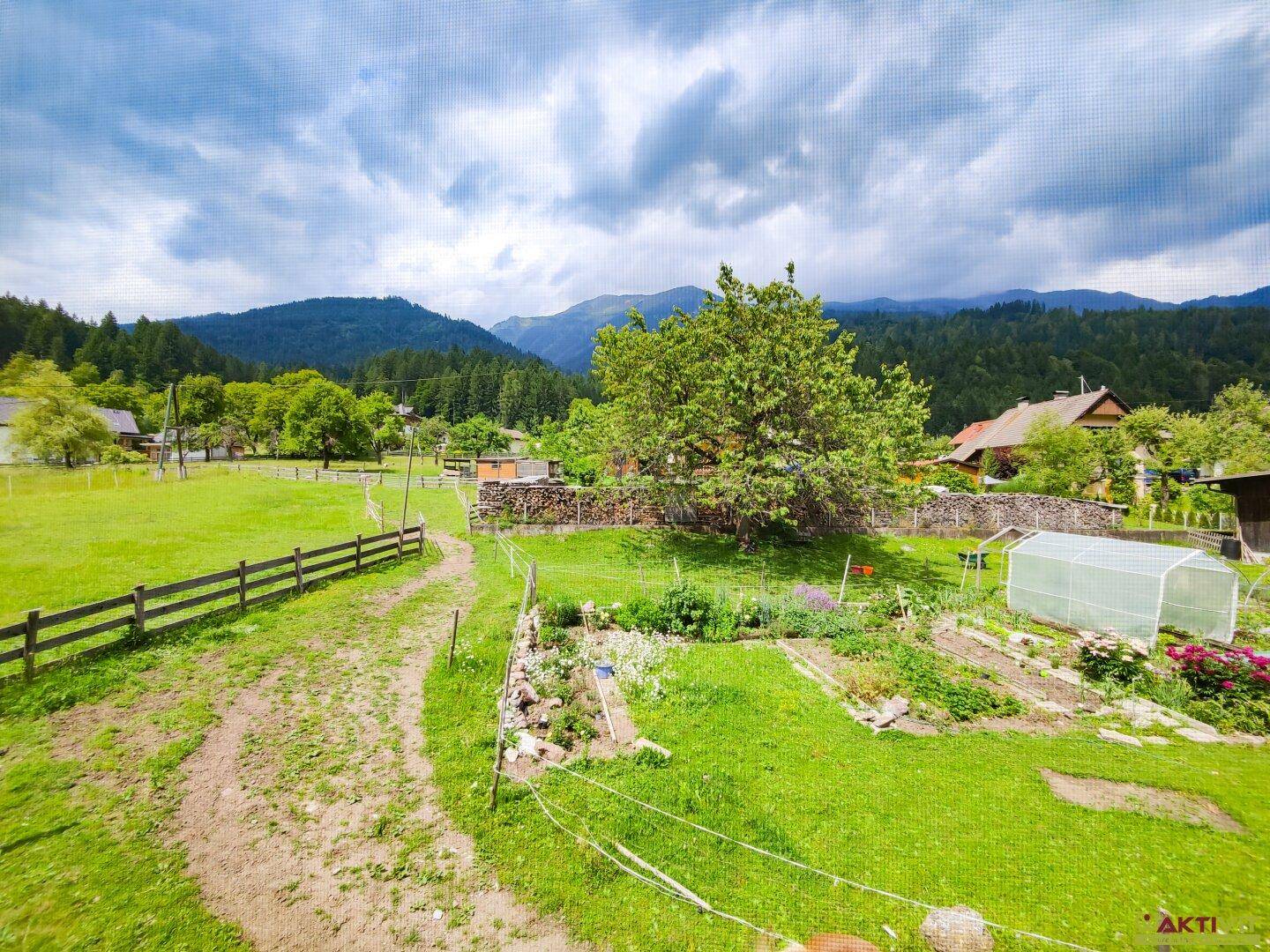 Großer Garten mit Rasenflächen, Gemüsegarten und Blick auf die bewaldeten Berge.