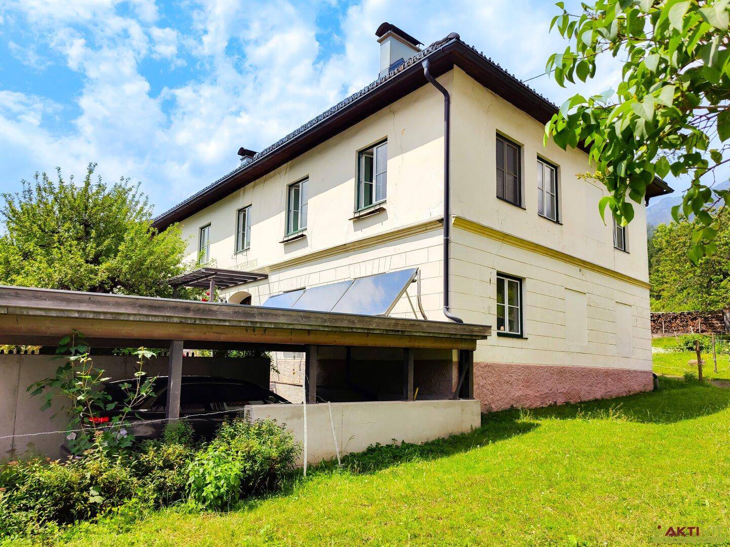Traditionelles Haus mit Carport und Solaranlage auf dem Dach, umgeben von grünem Rasen.