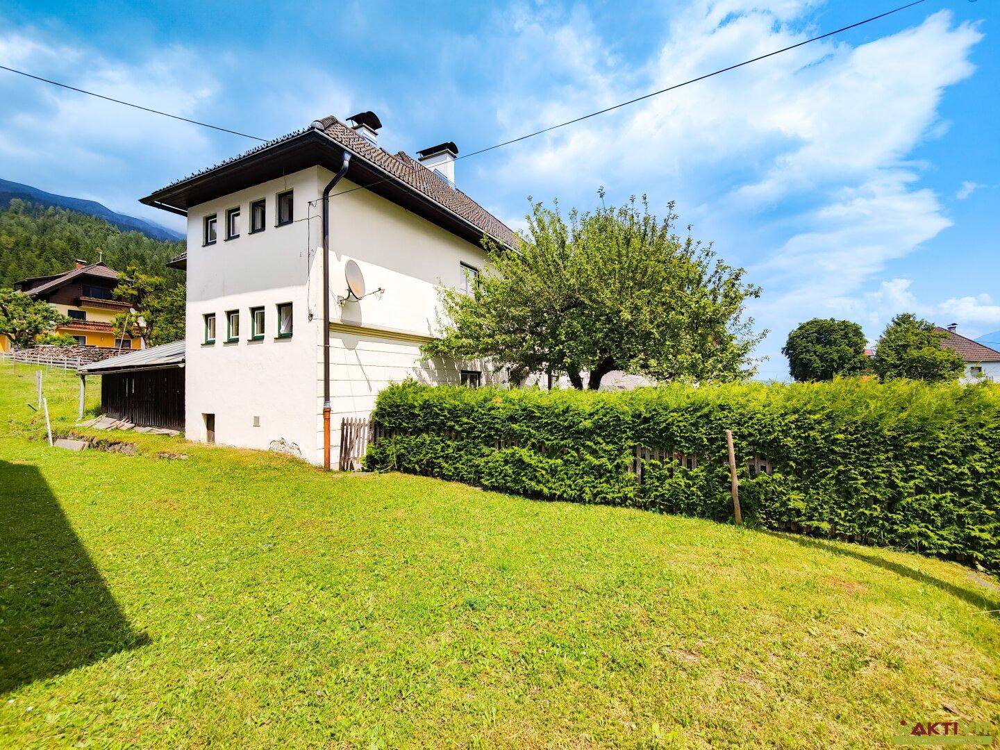 Rückseite des Hauses mit weitläufigem Rasen, gepflegter Hecke und Bergblick.