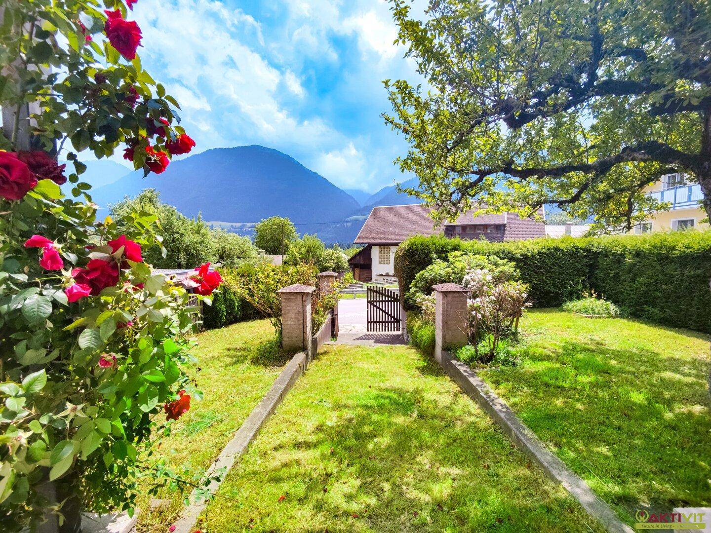 Malerischer Gartenweg mit blühenden Rosen und weitem Blick auf die umliegenden Berge.