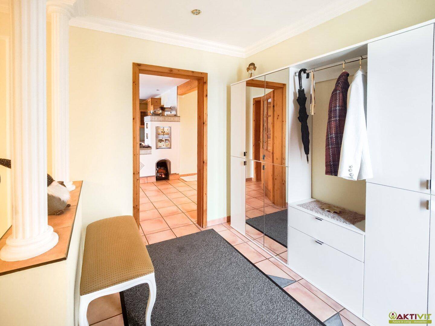 Heller Eingangsbereich mit Garderobe, Spiegel und Terrakottafliesen, der zu weiteren Räumen führt.