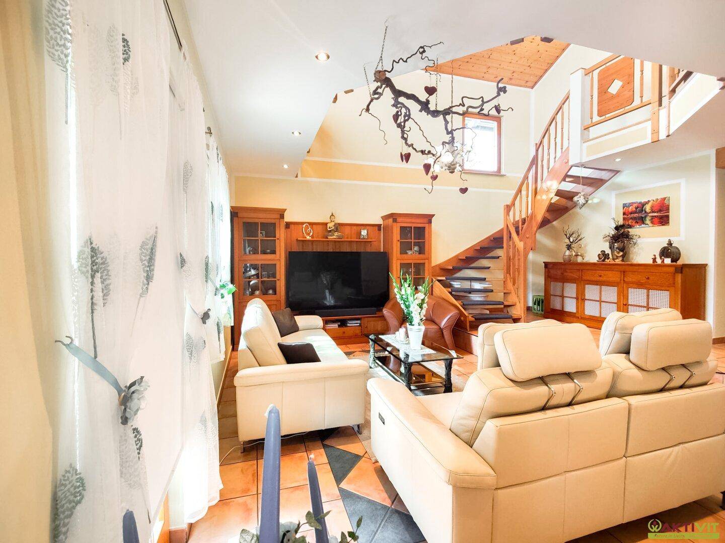 Geräumiges Wohnzimmer mit beigen Ledersofas, Holzelementen und einer offenen Galerie im Obergeschoss.