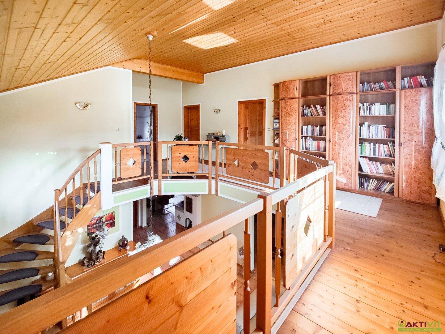 Heller Flur im Obergeschoss mit Holzfußboden, Bücherregalen und Blick auf den unteren Wohnbereich.