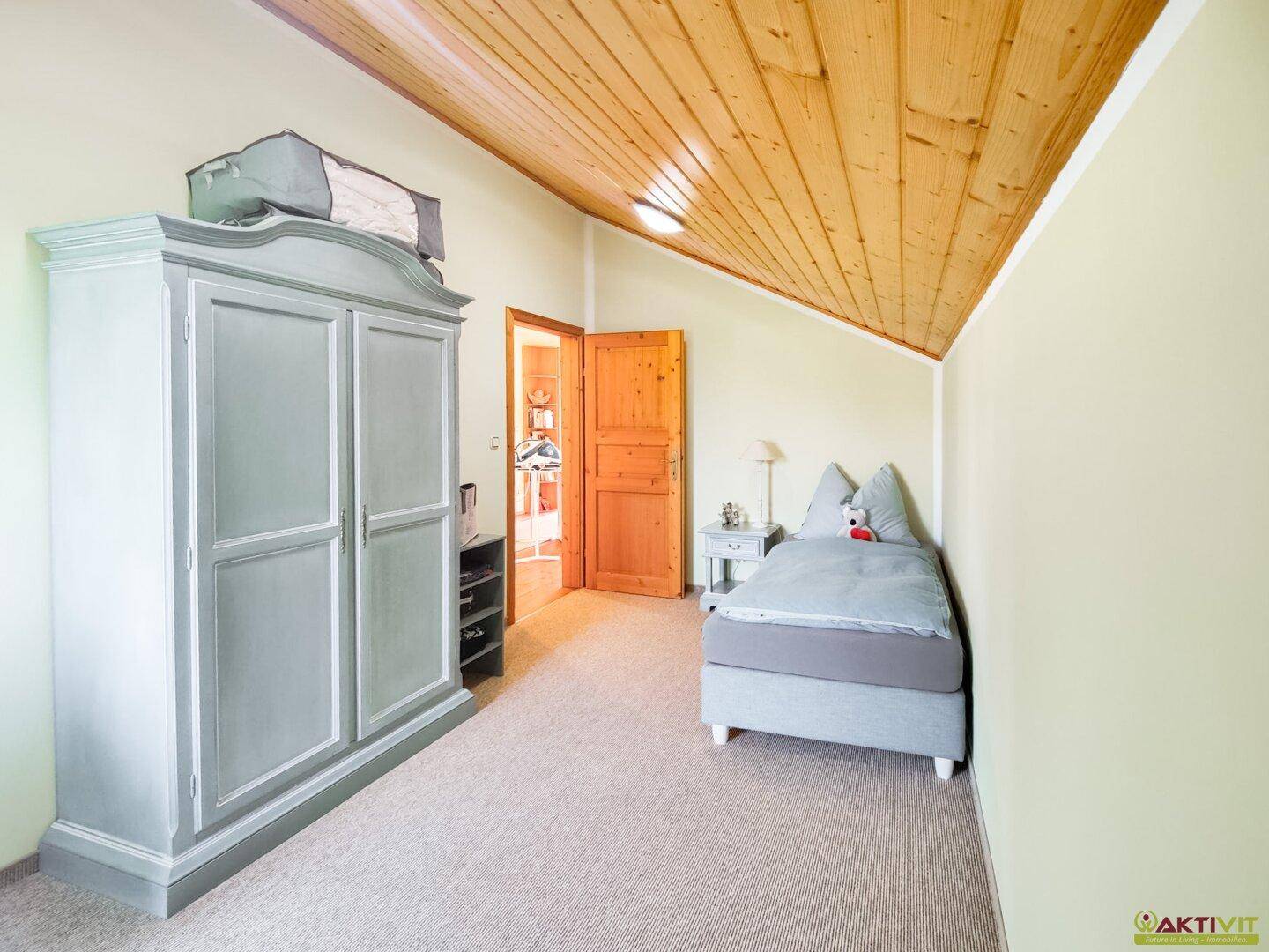 Helles Schlafzimmer mit Teppichboden, Dachschräge und einem großen Kleiderschrank in Pastellfarbe.