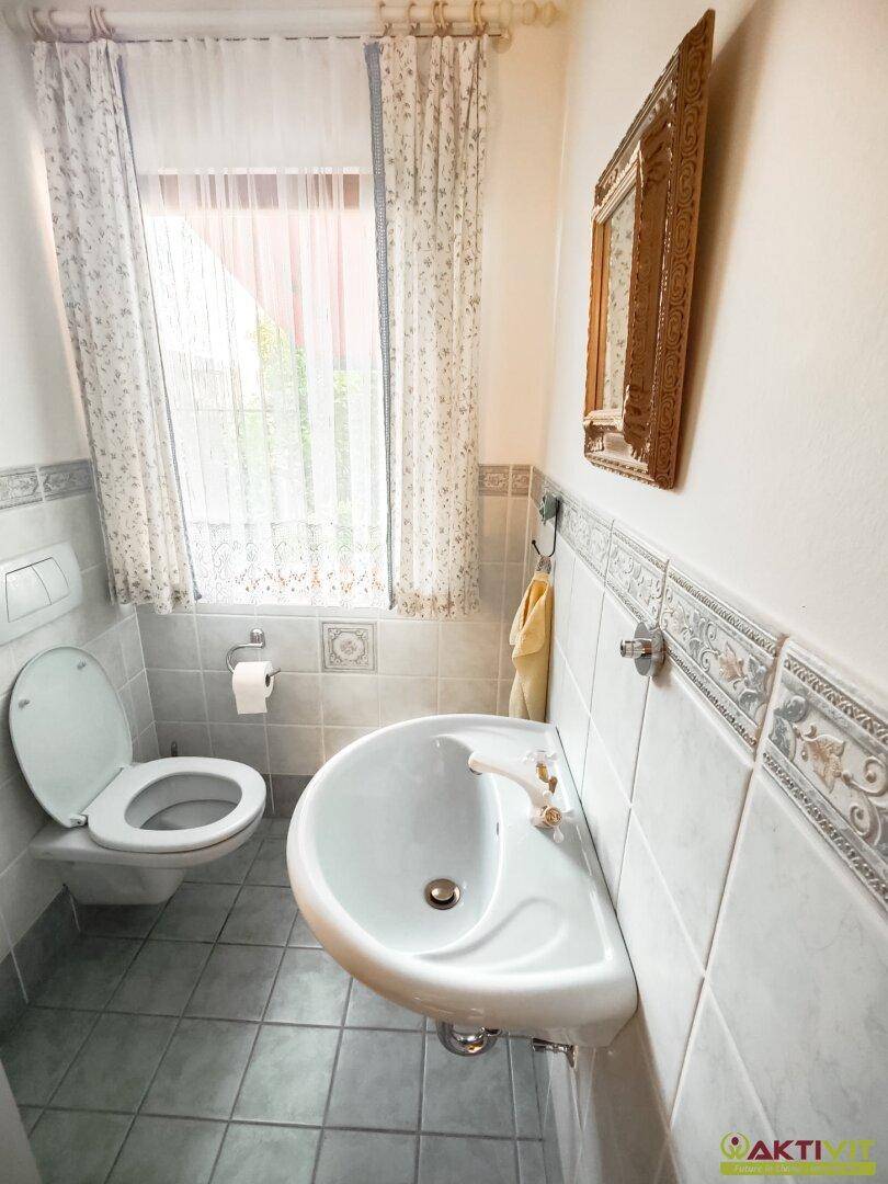 Kleines Gäste-WC mit Fenster, Wand-WC und einem halbrunden Waschbecken.