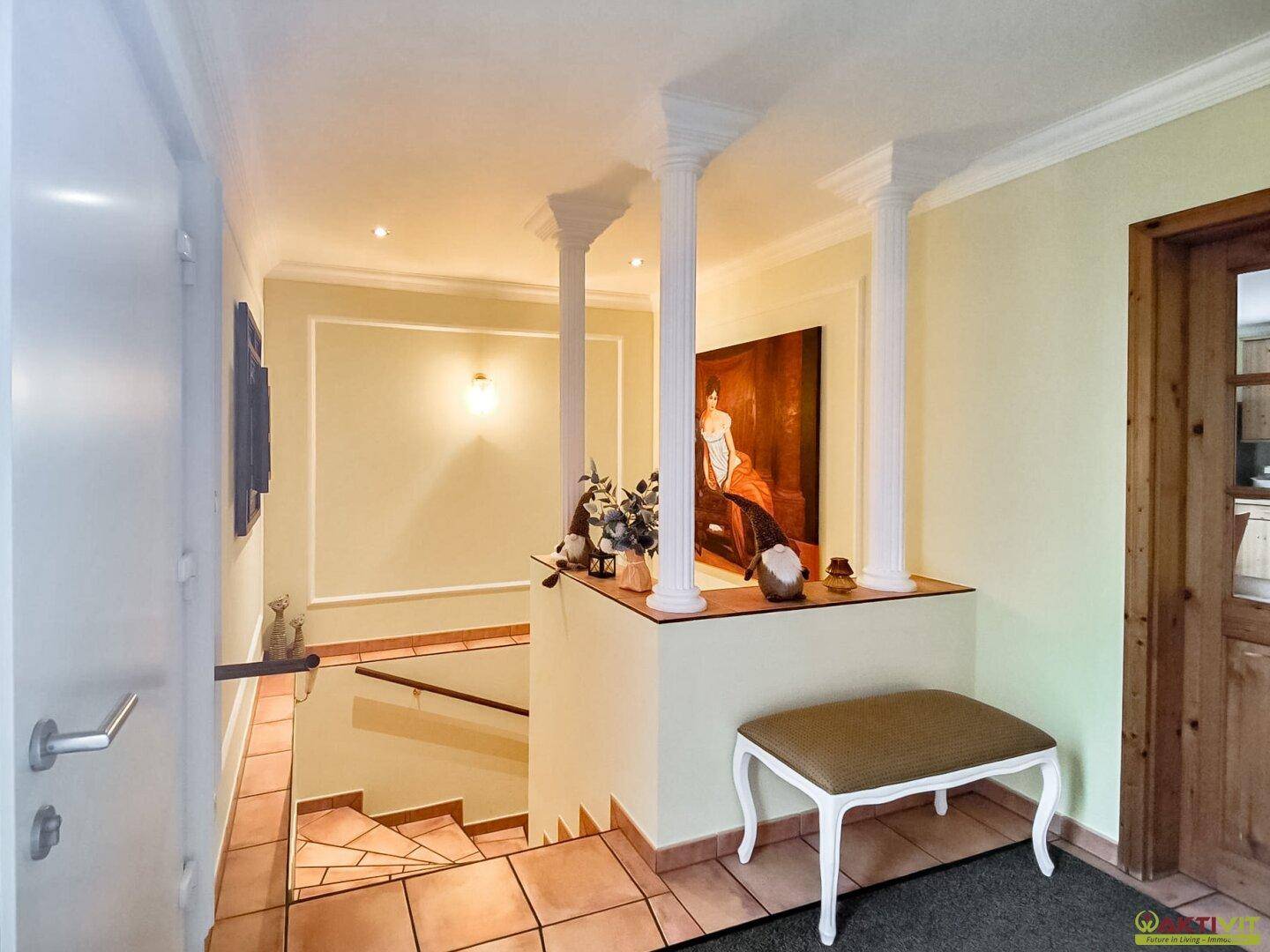 Heller Flur mit Säulen, Terrakottafliesen und einem Blick auf die Treppe zum Untergeschoss.