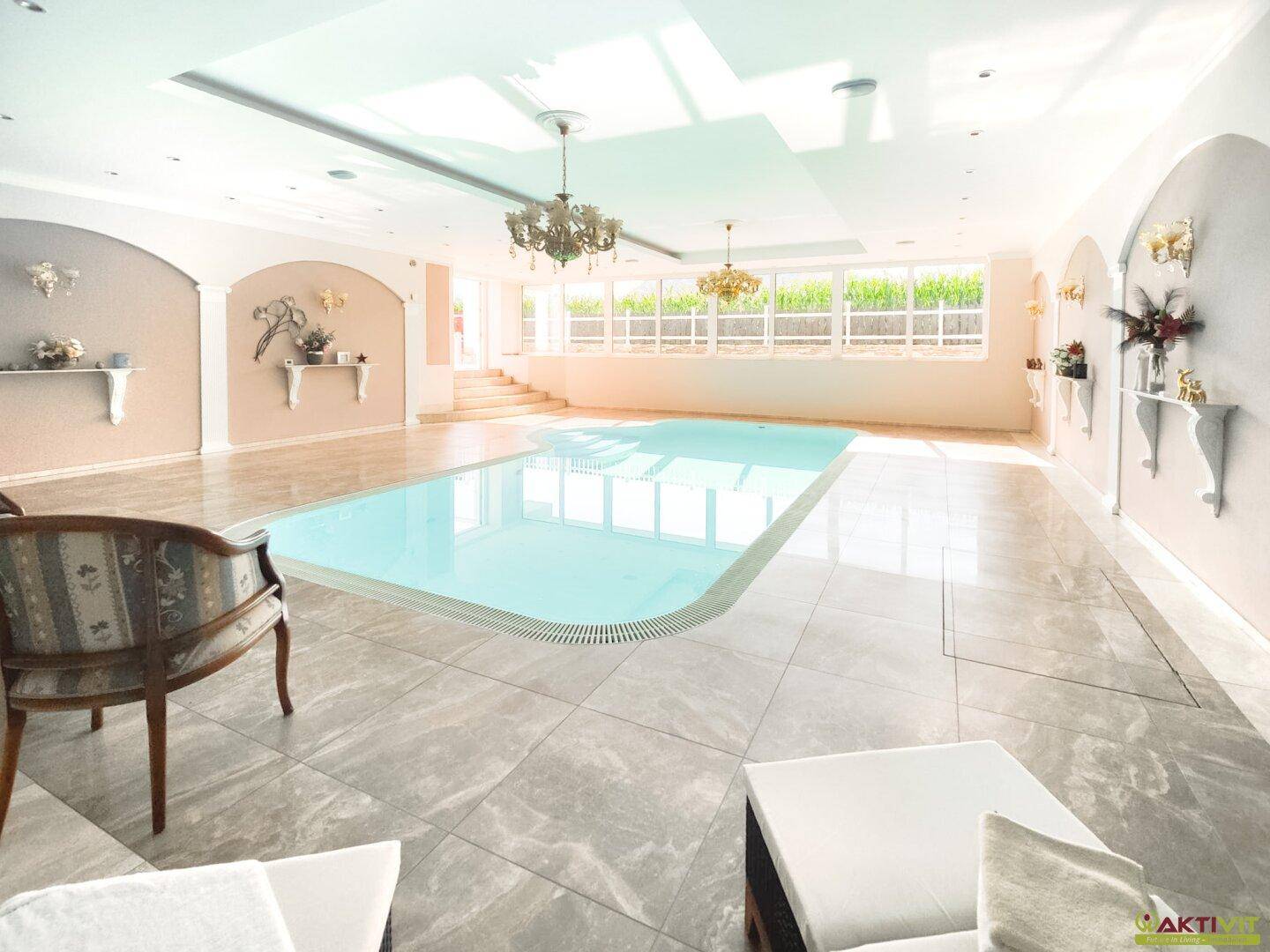 Luxuriöser Innenpoolbereich mit großen Fenstern, Marmorfliesen und eleganten Kronleuchtern.