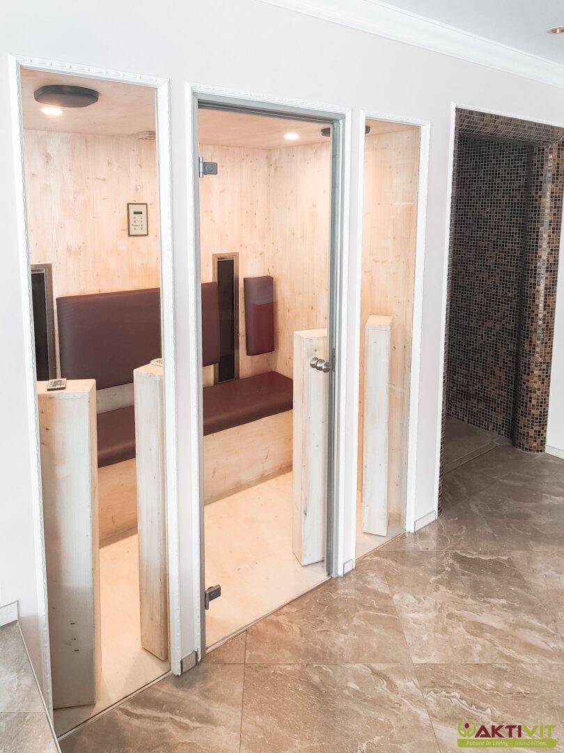 Moderne Sauna mit Holzbänken und Glastür, Teil eines luxuriösen Wellnessbereichs.