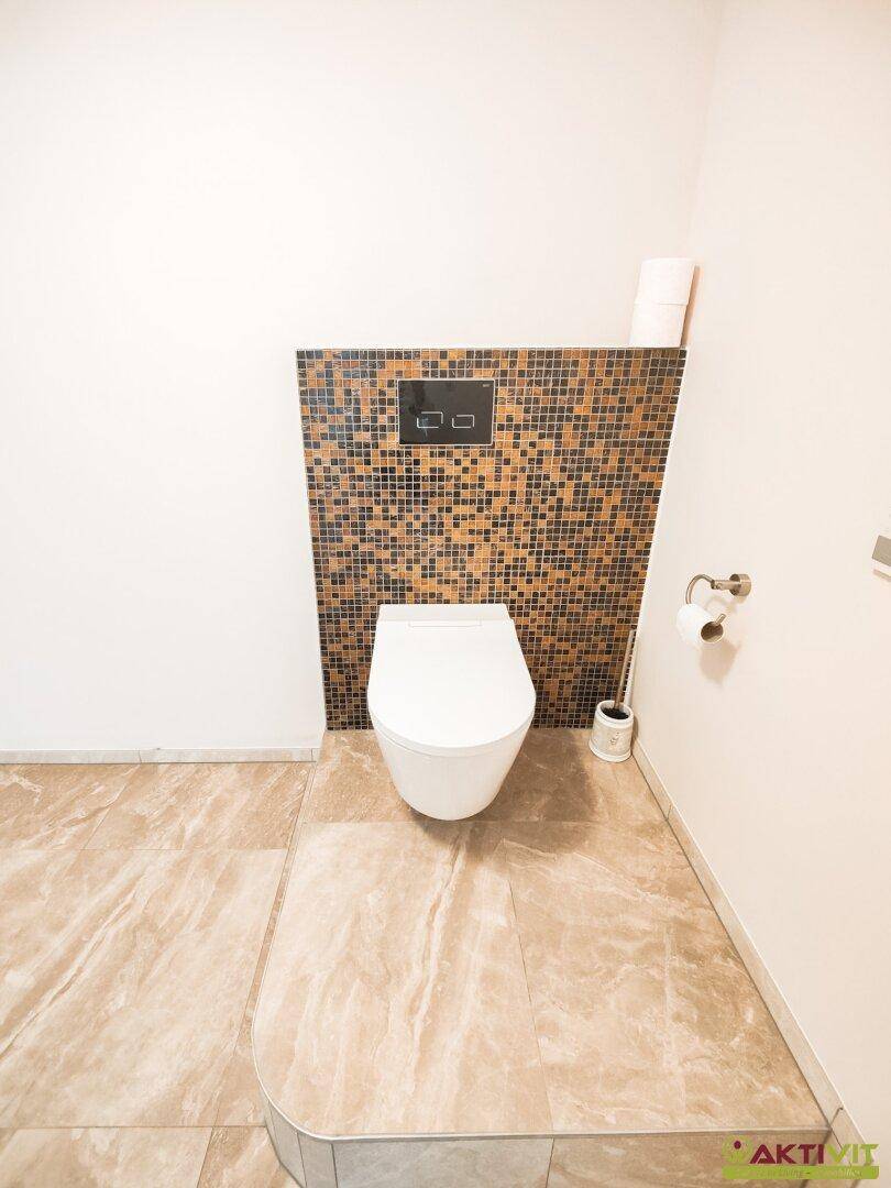 Modernes WC mit Wand-WC und Mosaikfliesen an der Wand, passend zum Wellnessbereich.