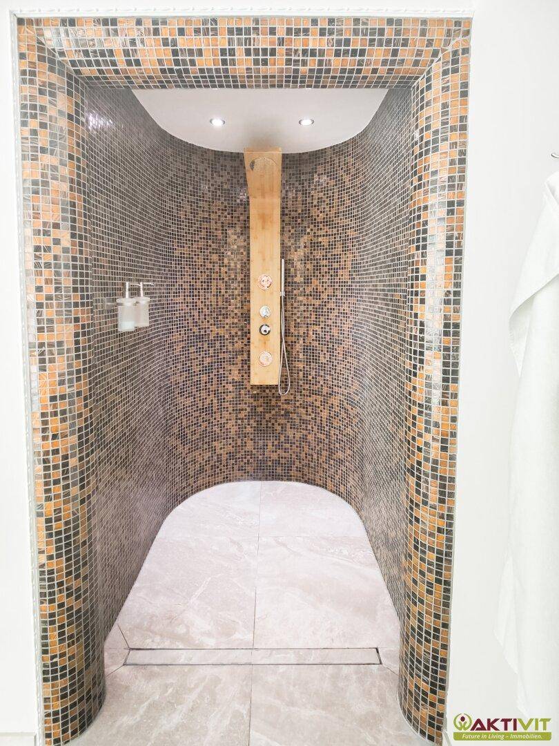 Großzügige Erlebnisdusche mit Mosaikfliesen und Holzpaneel, Teil eines luxuriösen Wellnessbereichs.