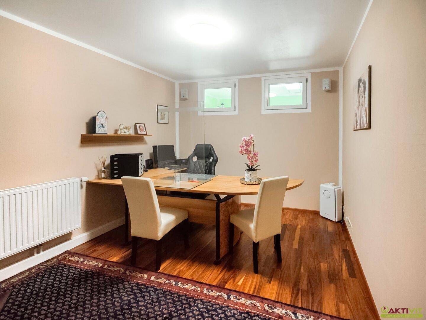 Helles Büro mit Holzboden, zwei Fenstern und einem großen Schreibtisch für produktives Arbeiten.