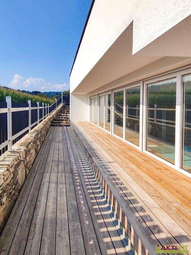 Moderne Terrasse mit Holzdeck und großen Glasfronten, die einen weiten Blick in die Landschaft bietet.