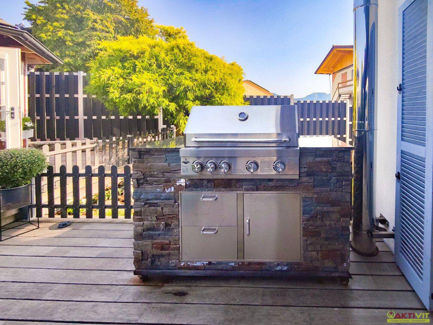 Außenküche mit integriertem Grill und Steinfassade auf einer Holzterrasse für gesellige Abende.