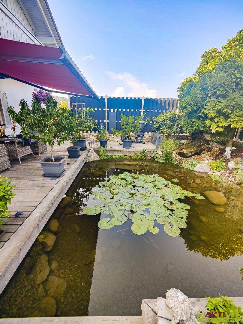Idyllischer Teich mit Seerosen, umgeben von einer Holzterrasse und üppigen Topfpflanzen.
